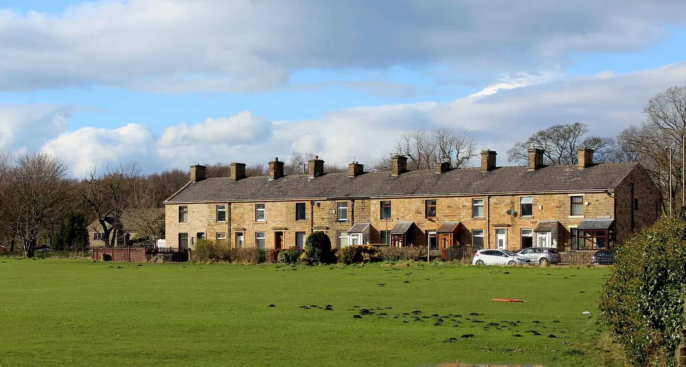 A row of stone terraced cottages on Padiham Road, Burnley, beside an open green