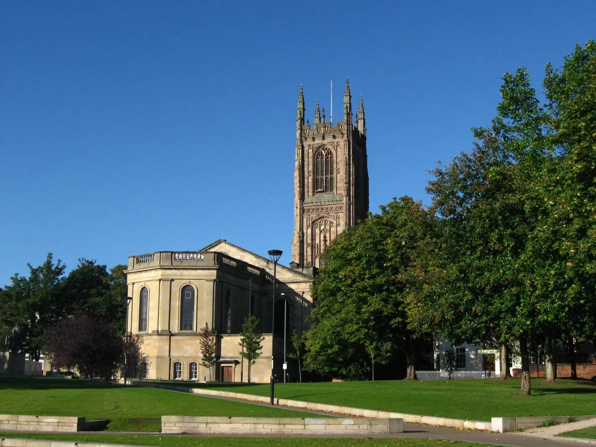 The Gothic tower of Derby Cathedral above Cathedral Green under a clear blue sky