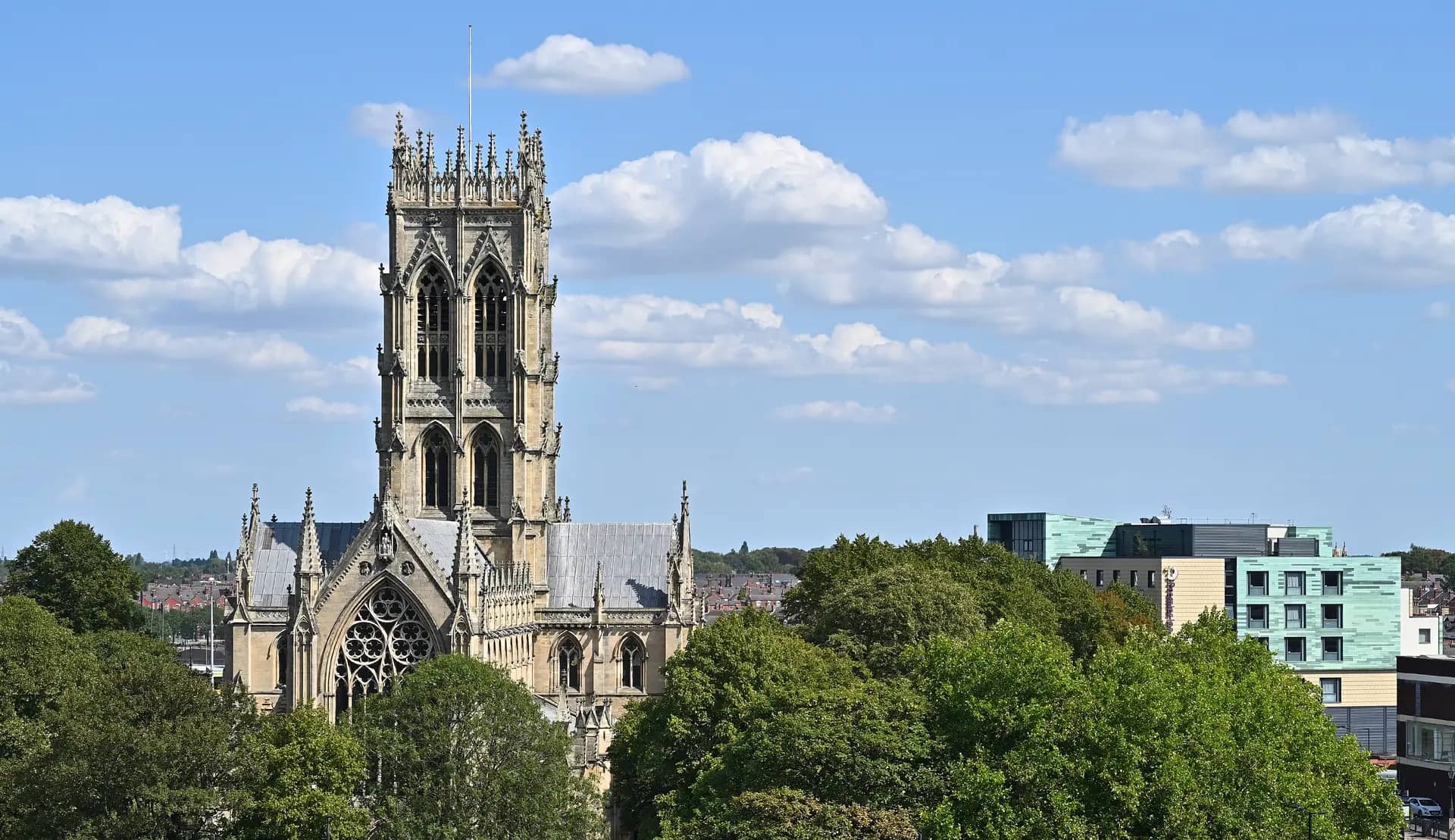 The tall tower of Doncaster Minster rising above trees and the town's rooftops on a sunny day
