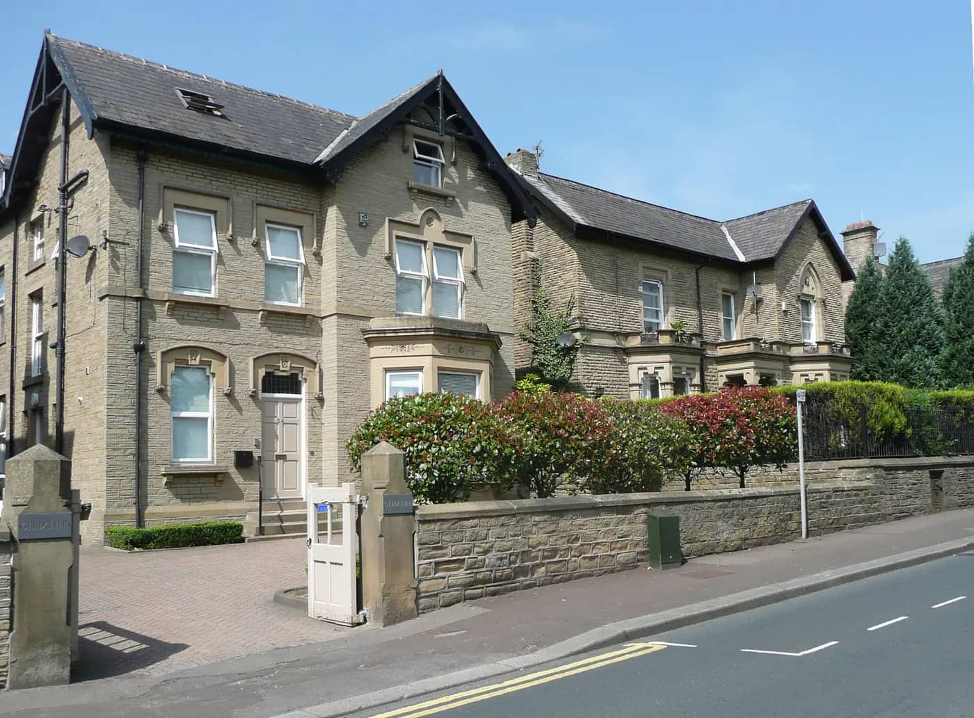 Victorian stone houses behind a garden wall and hedges on Gledholt Road, Huddersfield