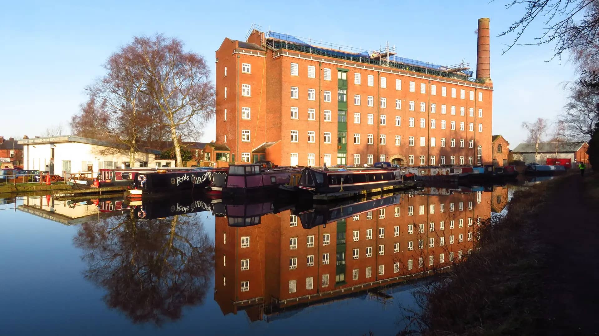 The red-brick Hovis Mill reflected in the Macclesfield Canal, with narrowboats moored alongside
