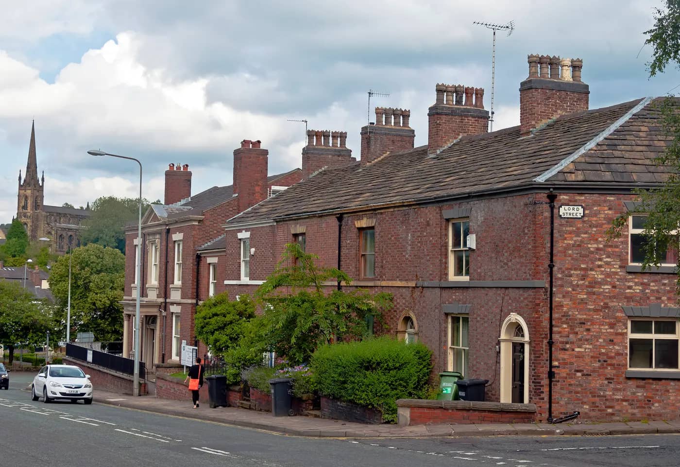 Brick terraced houses with stone-slate roofs on Sunderland Street, Macclesfield, with St Paul's Church spire behind