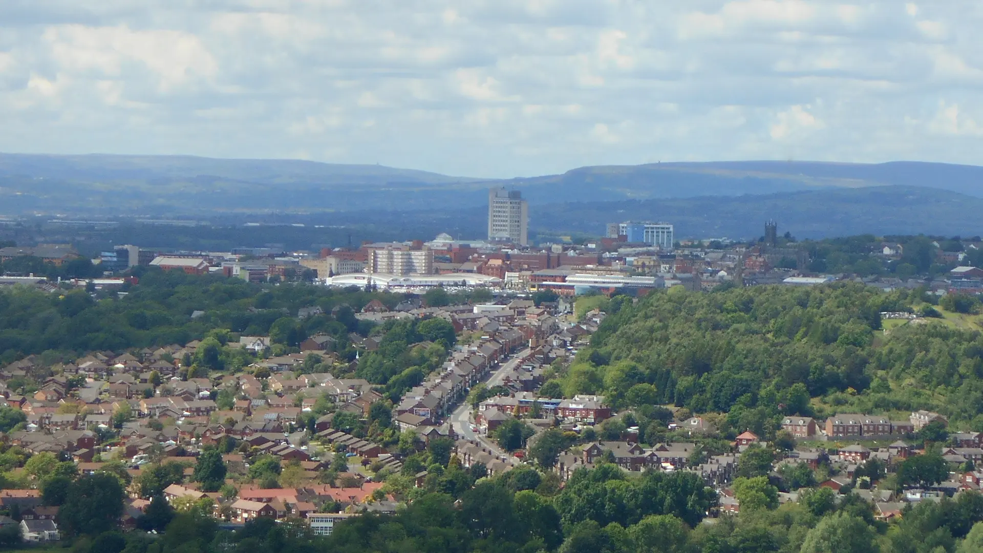 Streets of houses in Oldham stretching towards the town centre, with hills on the horizon, seen from Hartshead Pike