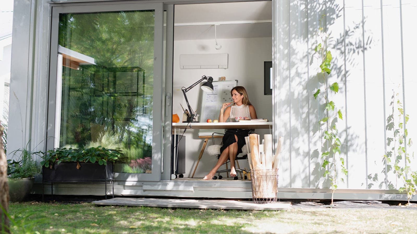 A woman working at a desk in a glass garden room with a Mitsubishi Electric wall unit above her