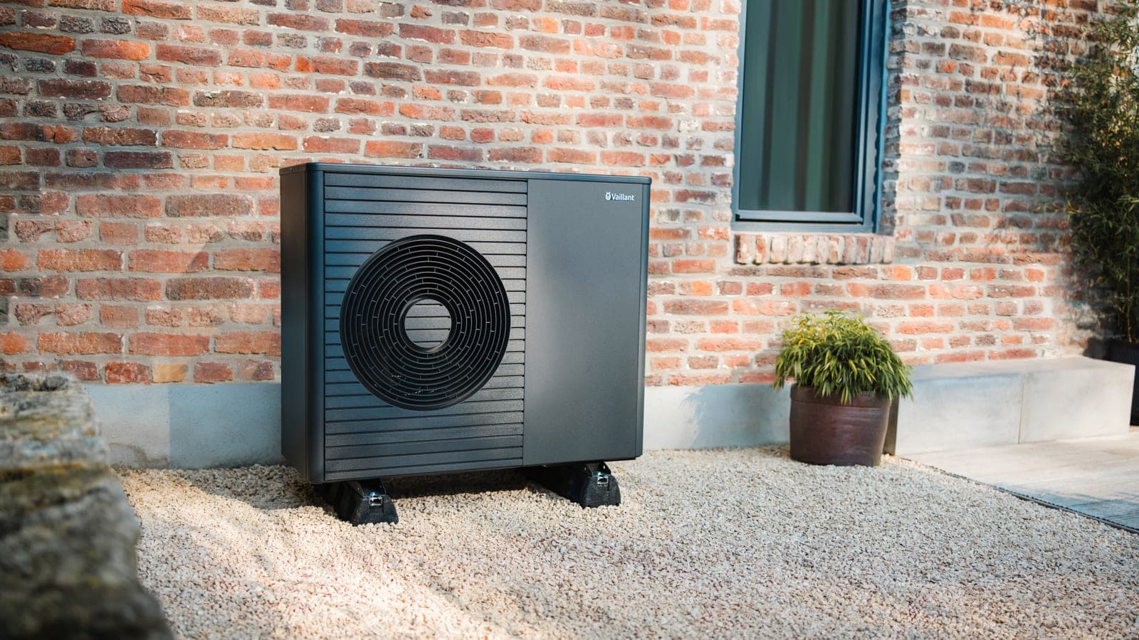 A Vaillant air source heat pump on gravel against the brick wall of a house