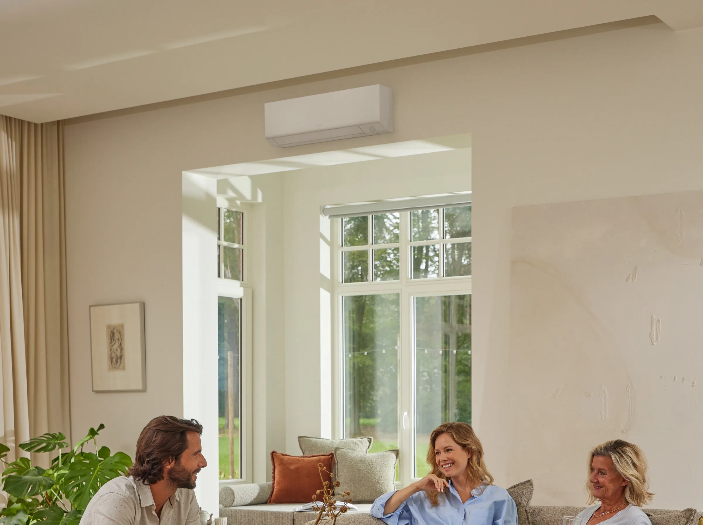 Three friends talking on the sofa in a bright living room with a Daikin wall unit above them