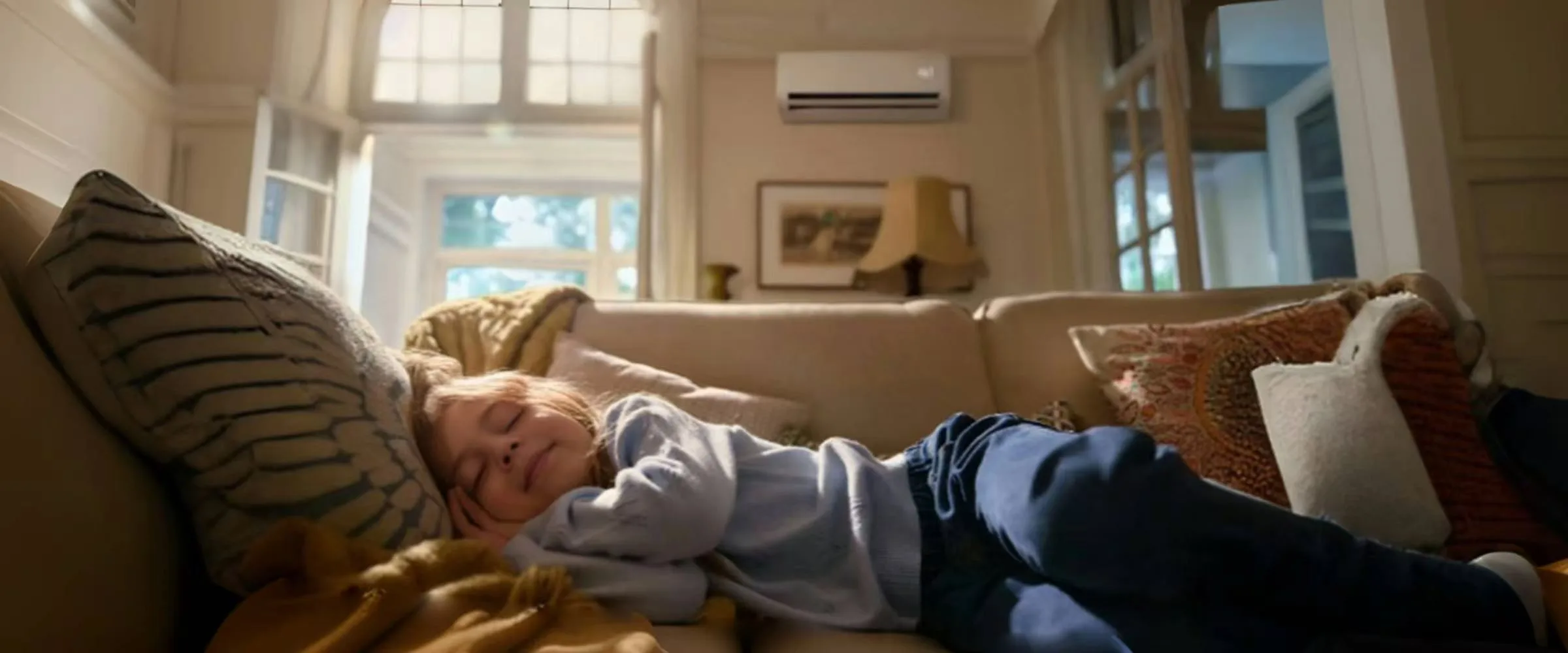 A child asleep on a sofa in a cosy living room with a Midea air conditioning unit on the wall