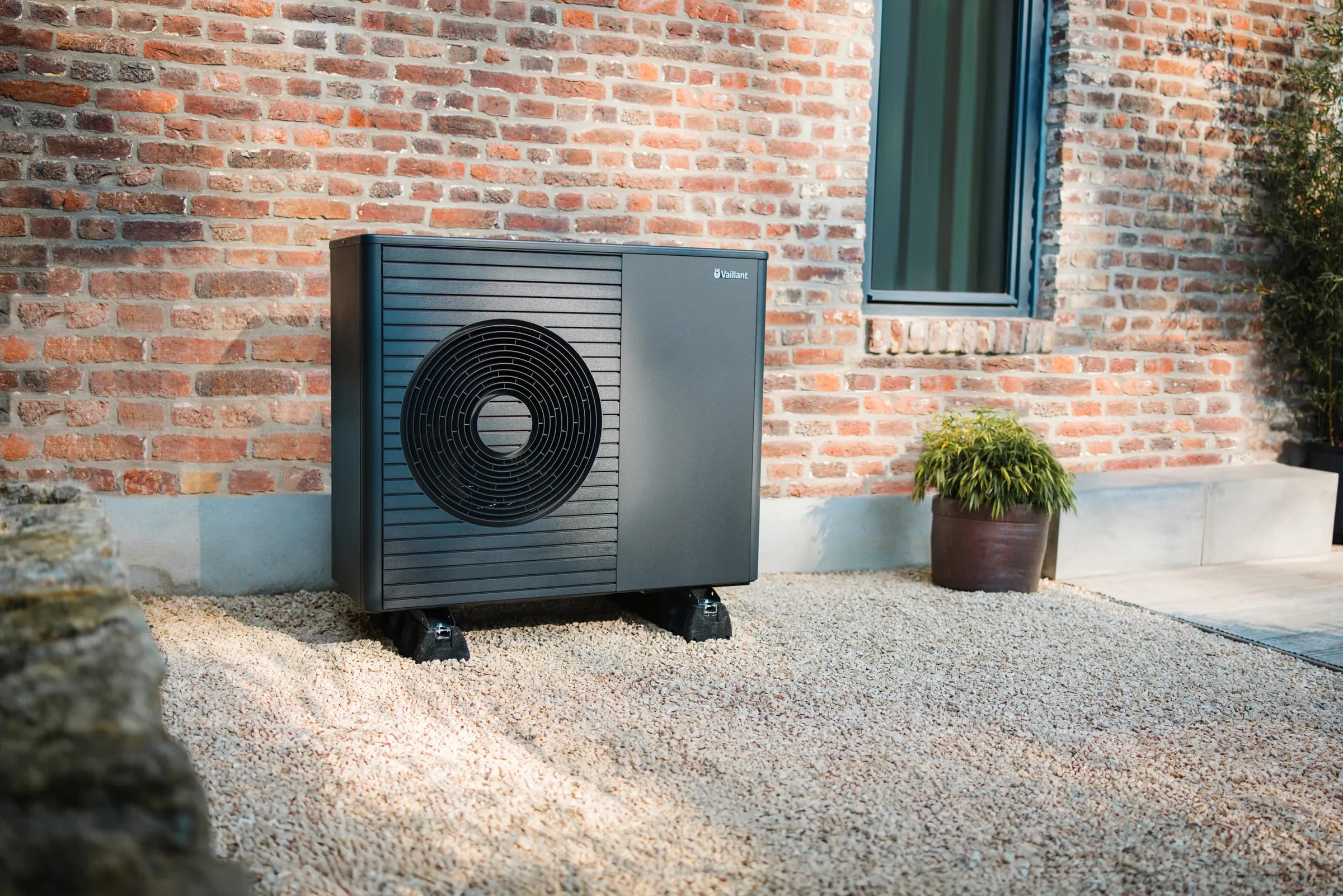 A Vaillant aroTHERM plus heat pump on gravel against the brick wall of a house