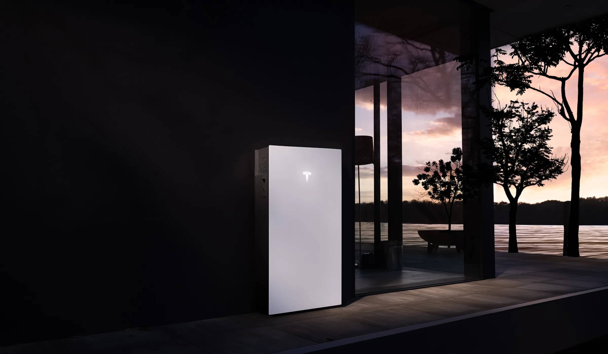 Tesla Powerwall 3 mounted on the outside wall of a glass-fronted house at dusk