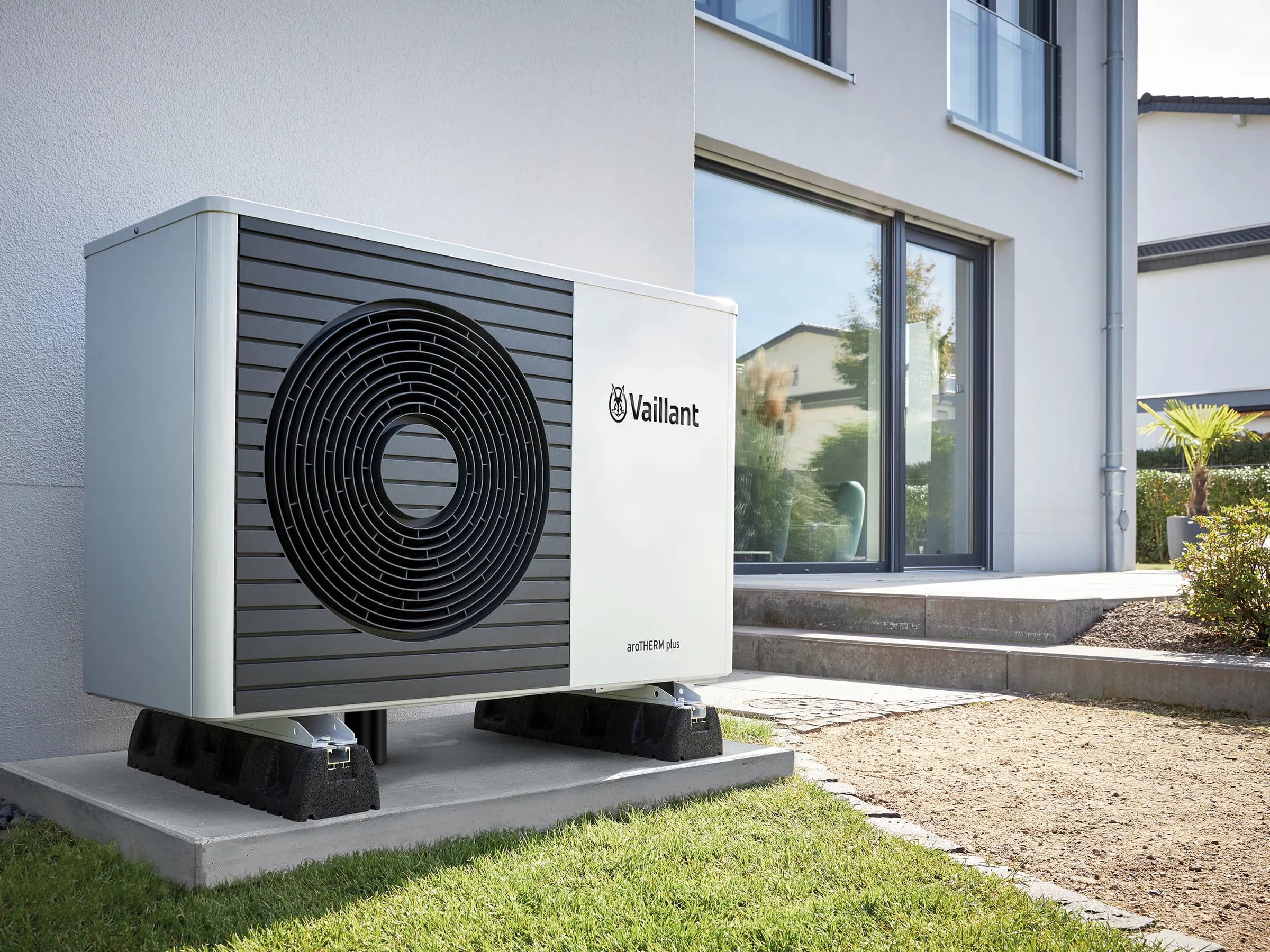 A Vaillant aroTHERM plus heat pump on a plinth beside a house