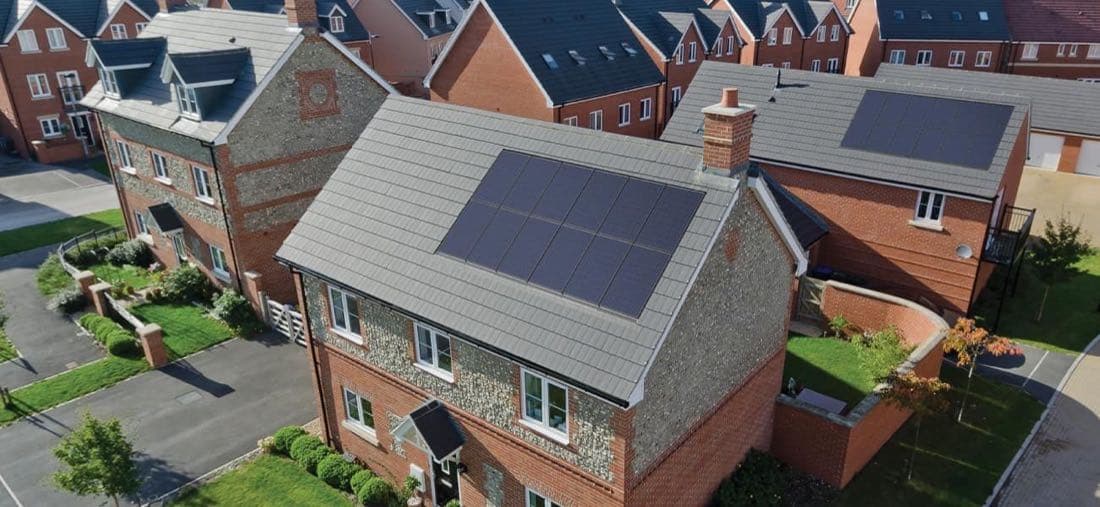 All-black solar array laid square on the slate roof of a brick and flint house, photographed from above